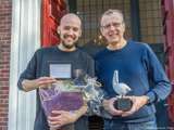 Twee glimlachende mannen houden de Pelikaan-prijs en een bos bloemen vast.