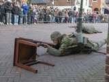 Verklede soldaten spelen toneelstuk op kerkplein bij Living History Appingedam, één soldaat ligt achter stoel met geweer.