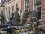 Verklede mensen staan tegen muur met soldaten bij Living History Appingedam.