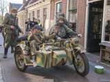 Verklede mensen rijden door straat met oude oorlogsmotor bij Living History Appingedam.