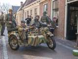 Verklede mensen rijden door straat met oude oorlogsmotor bij Living History Appingedam.